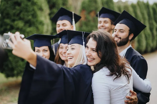 Multiethnic university graduates celebrating their achievement in a sunny park, sharing happiness and positive memories. They are smiling and taking a selfie.