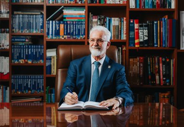 Experienced, confident, mature rector poses among shelves of books in a library, conveying authority and successful academia. clipart