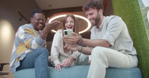 Três Colegas Multirraciais Sentados Sofá Limiar Assistindo Vídeos Engraçados Telefone — Vídeo de Stock