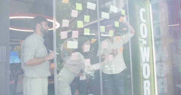 多样化的团队在一个协作的工作空间中头脑风暴业务理念 计算项目成本 并计划公司的成长 他们在办公室的玻璃墙上贴着便条 — 图库视频影像
