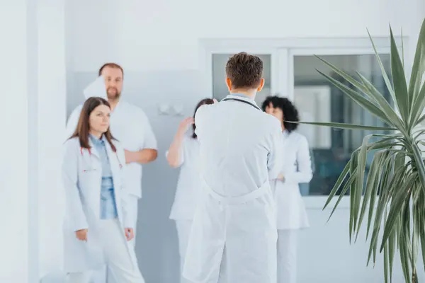 Group of experienced doctors confidently walking through a hospital hallway in medical uniforms and discussing.