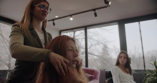 发型师工作室里的生姜姑娘准备做头发 和理发师讨论发型师的风格 以及卡车司机的动作 — 图库视频影像