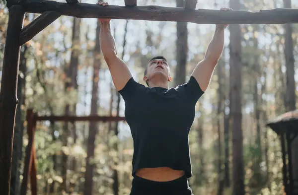 A happy, healthy male sportsperson enjoys a sunny day doing pull ups outdoors in a green forest. Embrace the fresh air and active lifestyle with this energetic image.