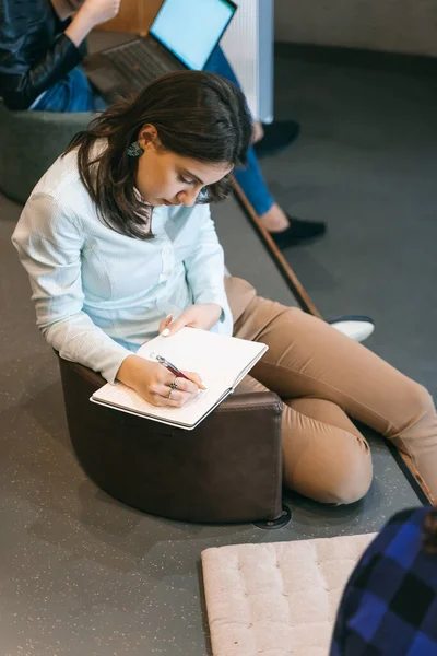 Female employee writing notes down in a notebook during presentation at work. Above photo