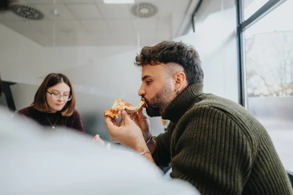 Young business team enjoys lunch break, discussing, eating pizza. Successful coworkers know the importance of taking breaks and refueling energy.