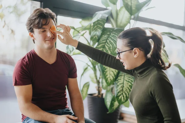 Colleagues playfully share a laugh during a work break, as a woman jokingly places an orange peel on her male coworkers eye.