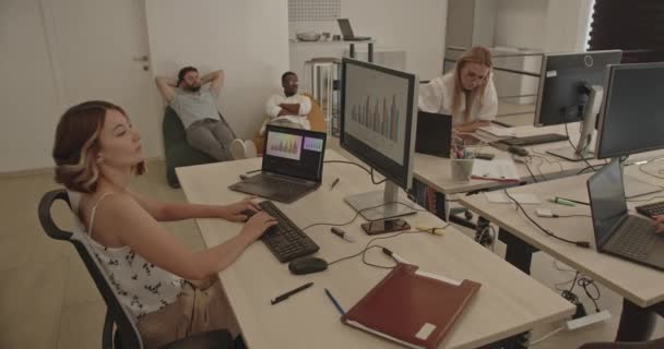 コンピューターで働く3人と 他の2人の同僚が居心地の良いオフィスソファーで休憩し 仕事から休憩している — ストック動画