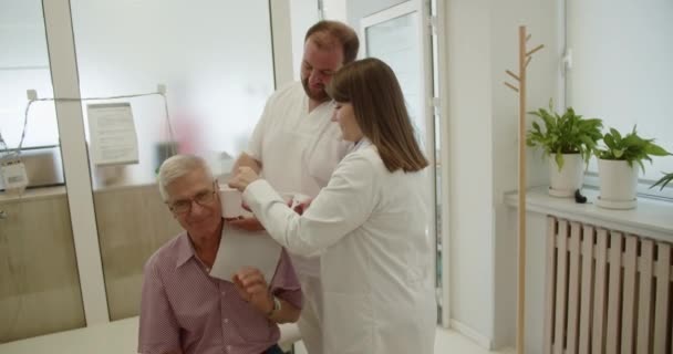 一名男医生和一名女医生正在向一名老年人提供医疗服务 他们正在给病人洗耳恭听 以改善他们的听力 — 图库视频影像