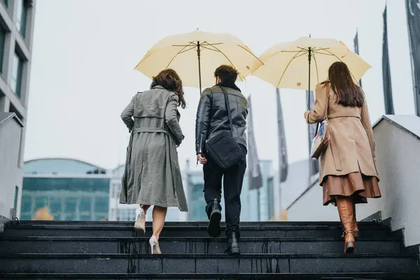 Friends sharing umbrellas walking up stairs in the city on a rainy day.