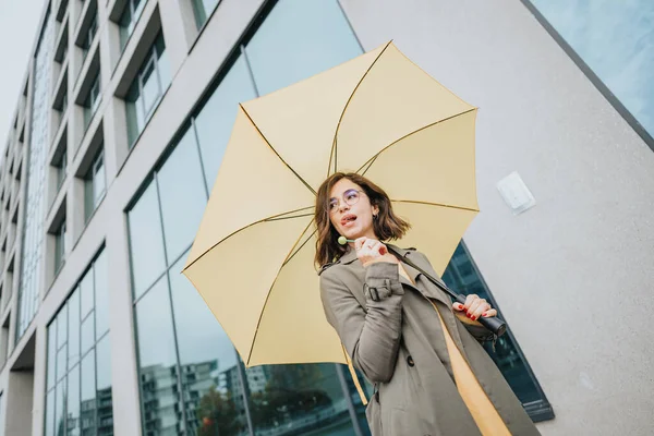 都市の設定で黄色の傘を持つスタイリッシュな若い女性 笑顔と楽しむ日 — ストック写真