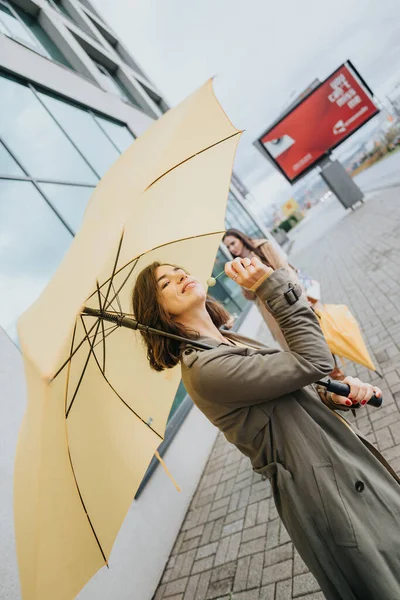 黄色い傘を持ったジョイフルな女性が街の通りでロリポップを楽しむ — ストック写真
