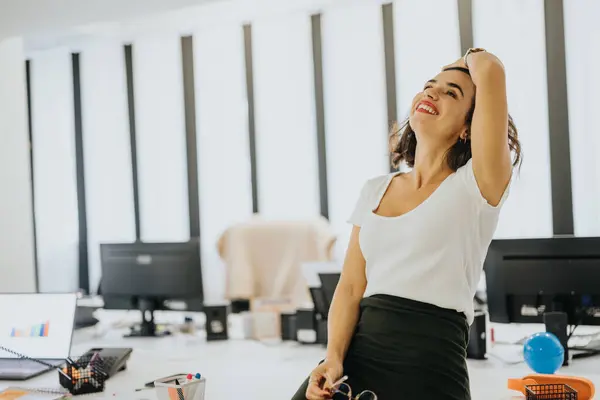 Joyful businesswoman stretching in a bright office, embodying job satisfaction and workplace happiness.