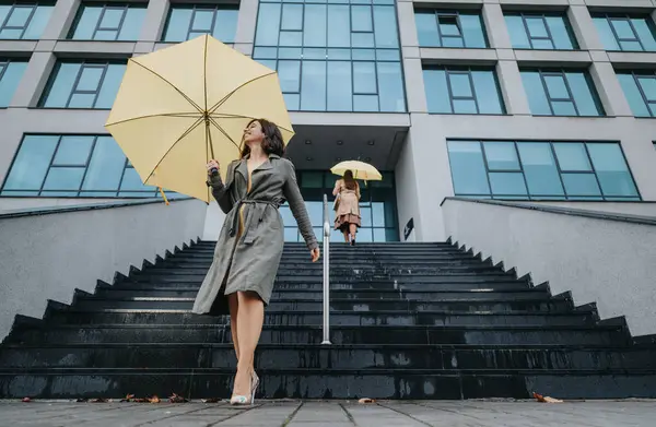 曇りの日に黄色い傘で階段を下って歩いている2人の女性 — ストック写真