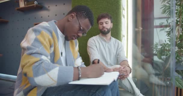 Bonito Preto Empregado Sexo Masculino Desenhando Seu Colega Branco Caderno — Vídeo de Stock