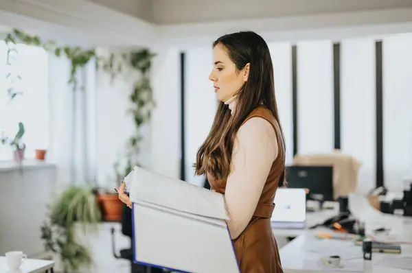Focused businesswoman carrying a box of belongings in an office, depicting change, relocation or new job.