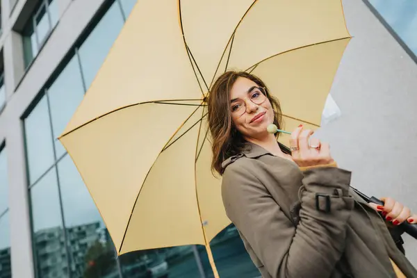 曇りの日に黄色い傘を持っているメガネを持つ笑顔の女性 — ストック写真