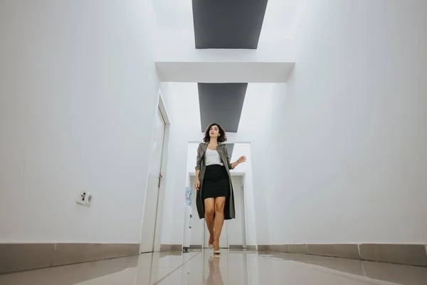 Elegant woman in business attire strides confidently down a brightly lit, modern office corridor, exuding professionalism and purpose.