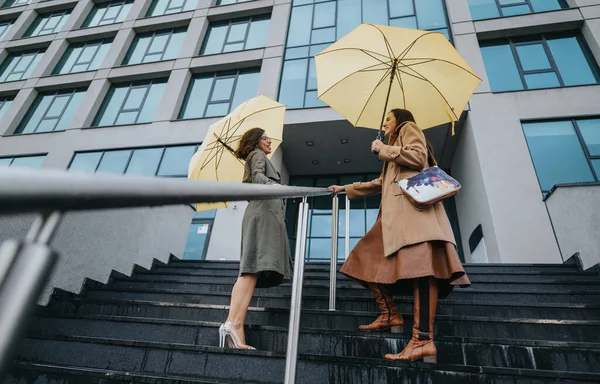 Městské Setkání Dvě Stylové Ženy Žlutými Deštníky Blízkosti Moderní Budovy — Stock fotografie
