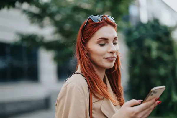 Gorgeous, redhead woman chatting on social medias with friends while walking on her way back home from work.