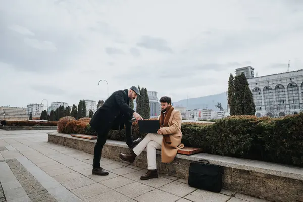Outdoor meeting between two well-dressed men sitting and chatting on a city bench with a calm, relaxed vibe.