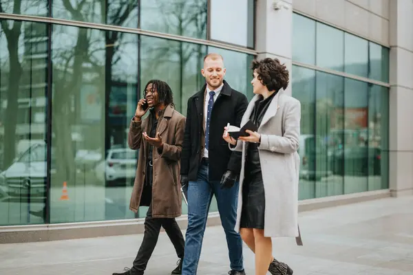 3人のプロのビジネス同僚が近代的なオフィスビルの外を歩きながら会話に従事し チームワークと多様性を示しています — ストック写真