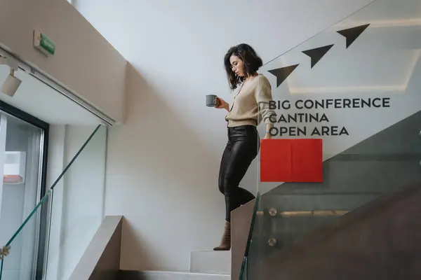 With caution, a businesswoman navigates down the stairs, balancing a cup of coffee in her hands.