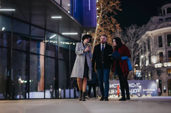 夜の照らされた都市の設定を歩きながら会話に従事する3人の専門家がチームワークと都市生活を紹介 — ストック写真