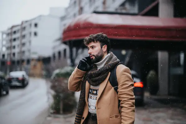一位穿着冬装 专心致志的商人一个人站在一个雪城街道上 展示了他的适应性 正在打一个很重要的电话 — 图库照片
