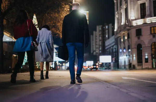 三人带着喜庆的装饰品和城市的灯火 在城市的人行道上散步的背景图 — 图库照片