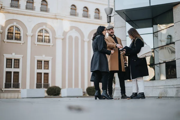 Three trendy adults engaging in a conversation on a city sidewalk, exchanging ideas with modern architecture and historical building in the background.