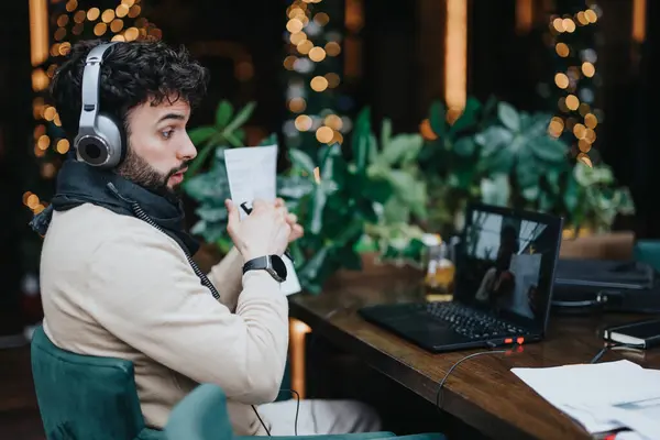 Young Bearded Businessman Headphones Intently Reviews Papers Bustling Cafe Surrounded — Stock Photo, Image