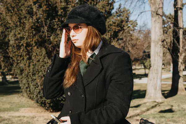 Creative young businesswoman engaging in a phone conversation while participating in an outdoor meeting during a sunny winter day in the park.