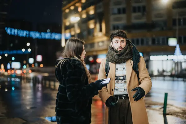 A young man and woman engage in conversation on a busy city street at night, illuminated by city lights and feeling of winter atmosphere.