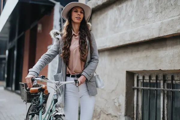 Elegant young woman with a bike strolls through the city. She exudes style and confidence with her fashionable outfit and hat.