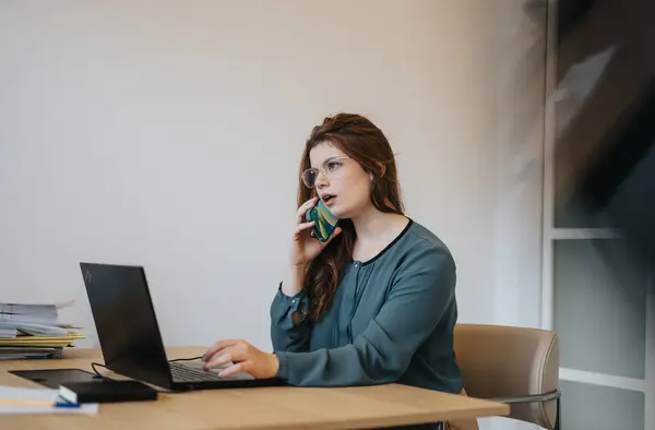 Woman looks confused during phone call while working on the lap top at the office.