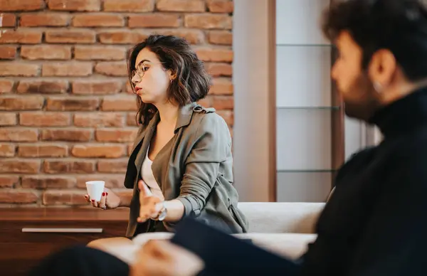 Focused young woman in conversation with male colleague in a casual office setting, expressing her point of view.