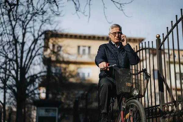 Active senior man taking a call while resting on a bicycle outdoors.