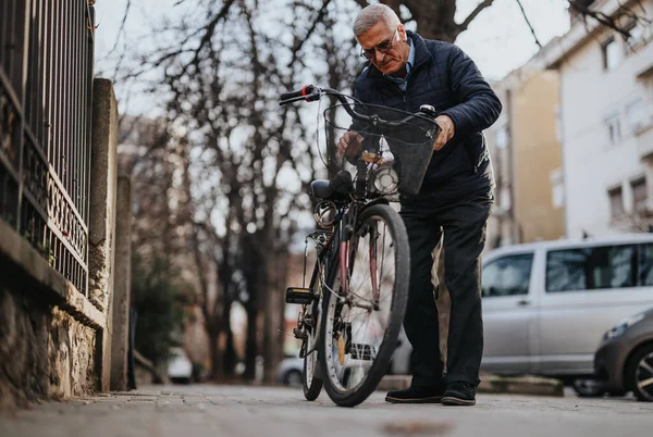 An older man is seen walking with his bicycle along a quiet urban street, reflecting an active and healthy lifestyle in the city.