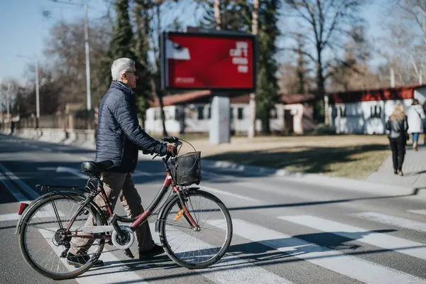 An elderly man walks with his bike beside a crosswalk in an urban setting, portraying active senior lifestyle and sustainable transportation.