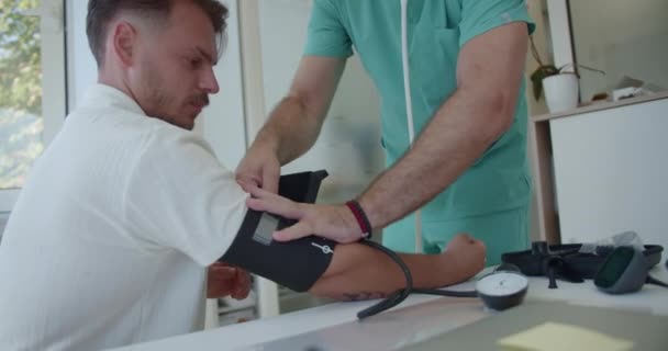 医生在诊疗室使用和配制血压计 他正在检查医院里一位年轻病人的血压 — 图库视频影像