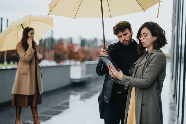 Dva Lidé Stylových Kabátech Sdílejí Deštník Prohlížejí Obsah Tabletu Zataženém — Stock fotografie
