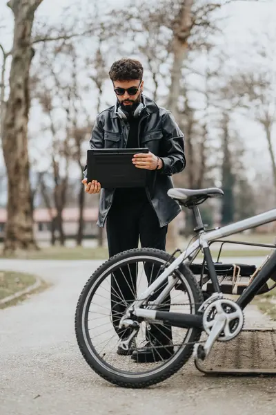 屋外のタブレットを使用したモダンでスタイリッシュなビジネスマン 公園の設定で自転車の隣に立って — ストック写真