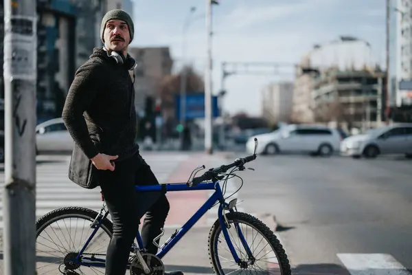 Молодой Городской Велосипедист Наушниках Повседневной Одежде Останавливается Перекрестке Голубым Горным — стоковое фото