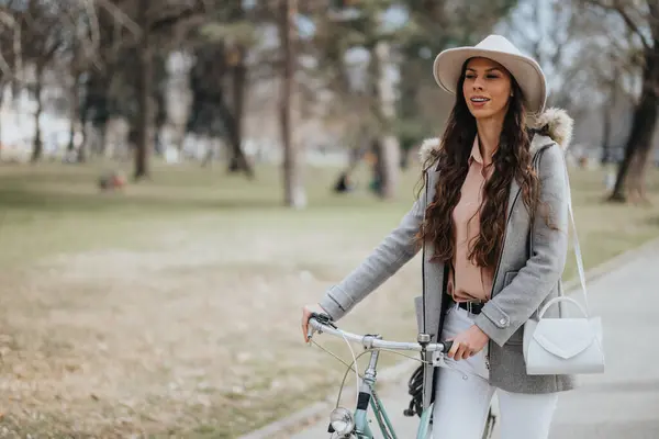 在城市公园里骑自行车的优雅女人 她戴着时髦的帽子和时髦的外套 体现了宁静的城市生活方式 — 图库照片