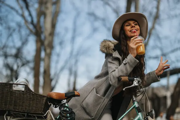 时尚的年轻女士在阳光灿烂的日子里喝着冷饮 在城市公园里休息一下 身边还有她的老式自行车 — 图库照片