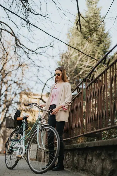 穿着休闲装 穿着复古自行车的优雅年轻女子在城市风景中穿行 体现了城市生活方式和可持续交通 — 图库照片