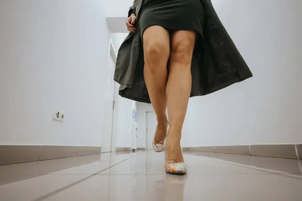 Low-angle shot capturing the movement of a sophisticated womans dress and high-heeled shoes while striding along a corridor.