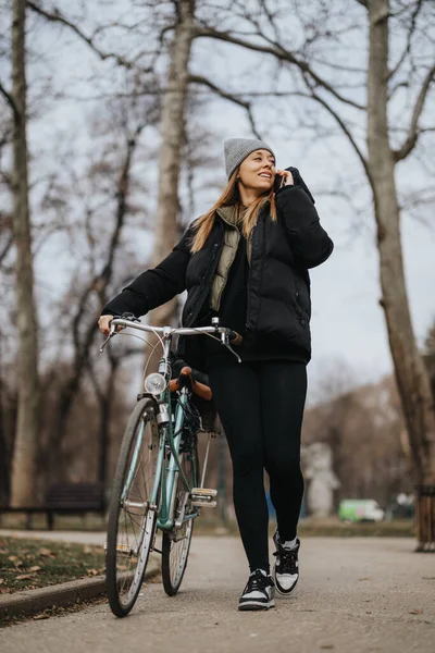Χαμογελαστή Γυναίκα Casual Ρούχα Μιλάει Στο Τηλέφωνο Ενώ Περπατάει Ποδήλατό — Φωτογραφία Αρχείου