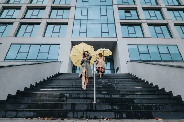 Dos Amigos Con Sombrillas Amarillas Bajando Escaleras Cerca Edificio Moderno — Foto de Stock