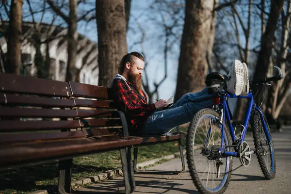 Odaklanmış Bir Işadamı Elinde Tabletle Bir Bankta Oturuyor Bisikleti Yanında — Stok fotoğraf